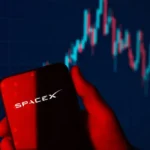 Phone displaying the SpaceX logo against a stock chart background, representing SpaceX stock performance, IPO price pressure, and investor sentiment.
