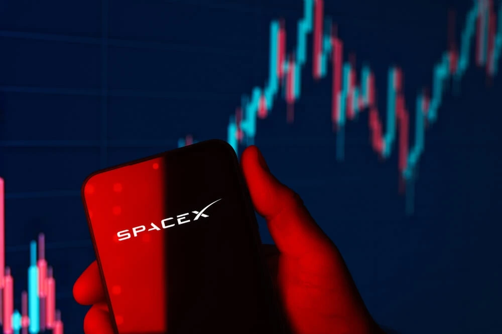 Phone displaying the SpaceX logo against a stock chart background, representing SpaceX stock performance, IPO price pressure, and investor sentiment.