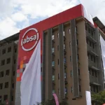 Photo of an Absa-branded office building with a large red Absa logo panel on the front facade. The image shows the bank’s corporate presence and is used to illustrate Absa Group’s planned sale of controlling stakes in First Assurance and Absa Life Assurance Kenya, while maintaining insurance distribution through Absa Bank Kenya.