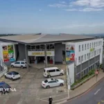A landscaped commercial property with palm trees, parked cars and a white building, used to illustrate Dipula Properties, South African listed property, retail property acquisitions and real estate investment trusts.
