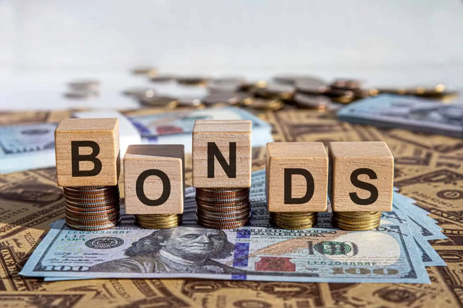 Wooden blocks spelling “Bonds” placed on stacks of coins and U.S. dollar notes, representing Treasury securities, fixed-income investing, bond yields and government-debt markets.