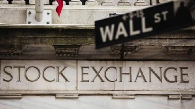 Article image showing the New York Stock Exchange building with a Wall Street sign in the foreground. The image represents U.S. equity markets, Wall Street trading sentiment and investor focus on the S&P 500 near record levels.